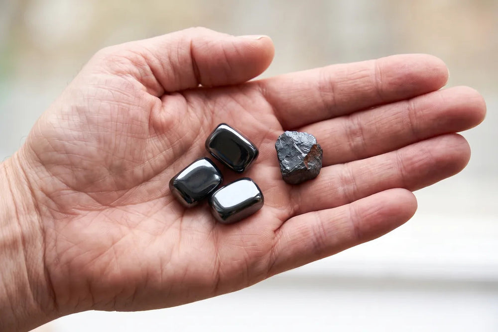 Polished black hematite tiles and a raw piece of hematite in a man's open hand