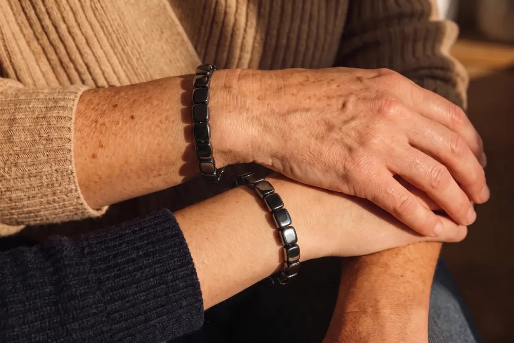 A father and his grown son with arms crossed, the same black bracelet on each wrist